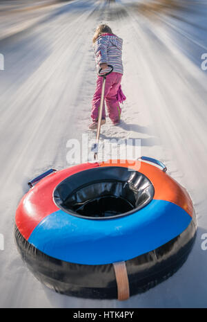 Petite fille tirant son tube gonflable coloré après une descente coulissante milou et colline glacée voie Banque D'Images