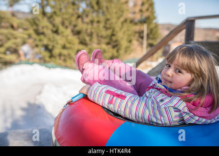 Petite fille prête à faire glisser la pente d'une colline glacée la neige et la piste d'un tube gonflable coloré Banque D'Images