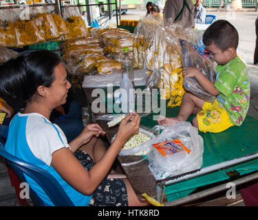 Bangkok, Thaïlande. 14Th Nov, 2006. Une femme strings pétales de fleurs pour faire les guirlandes électriques dans le célèbre marché aux fleurs de Bangkok (Pak Klong Talad) tandis que son jeune garçon joue sur sa table. La Thaïlande et le marché est devenu une destination touristique favorite. Credit : Arnold Drapkin/ZUMA/Alamy Fil Live News Banque D'Images