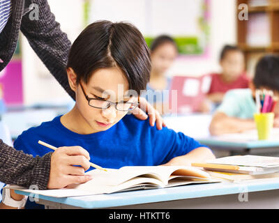 L'école primaire asiatique garçon obtention d'aide de l'enseignant en classe. Banque D'Images