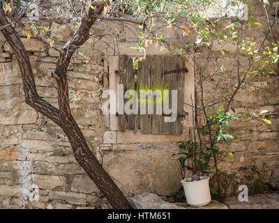 Une fenêtre en bois avec un vieux old rusty charnières charnière et volets persiennes en mur de pierre avec un arbre et plante en pot Croatie Banque D'Images