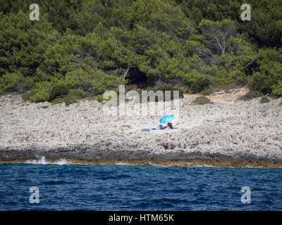 Un seul un seul sur un sunbather shingle stony isolé plage rocheuse à l'ombre d'un parasol parasol bleu dans le sud de la Croatie Banque D'Images