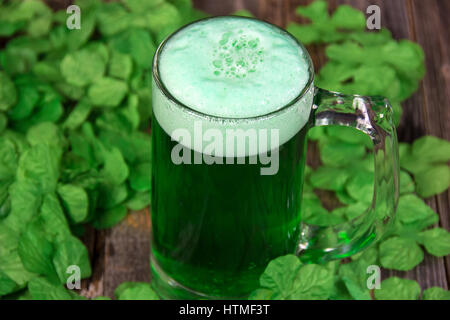 La bière verte écumeuse en tasse avec des trèfles irlandais sur bois Banque D'Images