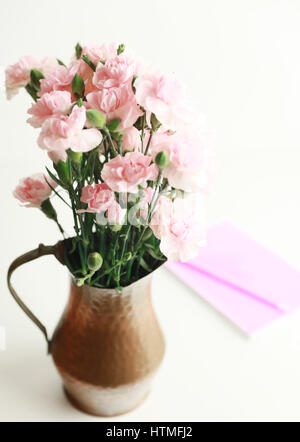 Une présentation verticale de vase en cuivre avec des œillets miniatures rose sur un fond blanc isolé avec un ordinateur portable rose. Banque D'Images