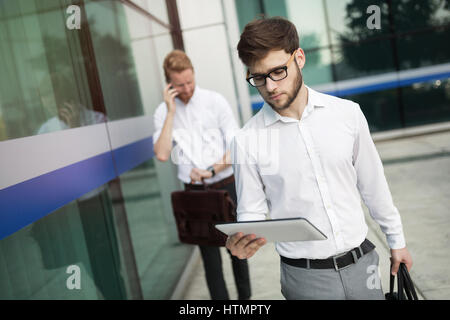 Les gens d'affaires la marche à l'extérieur et à l'aide de téléphones mobiles tablettes Banque D'Images