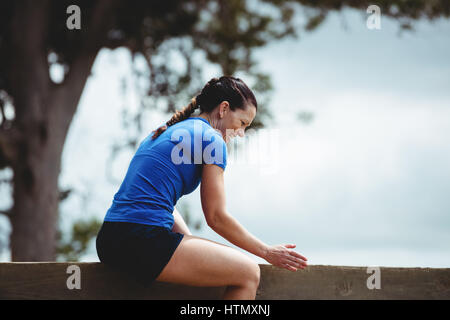 Fit woman sitting sur mur en bois obstacle dans boot camp Banque D'Images