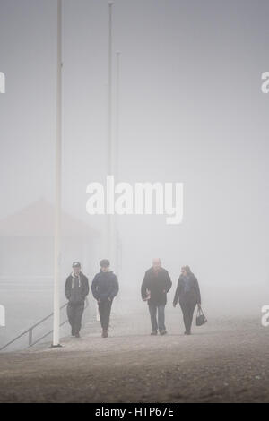 Aberystwyth, Pays de Galles, Royaume-Uni. 14Th Mar, 2017. Météo France : Les gens qui marchent le long de la promenade est obscurci par le brouillard dans la station balnéaire d'Aberystwyth, sur la côte ouest du pays de galles comme un épais manteau gris et froid de la brume de mer tourbillonnant en vient au large de la mer d'Irlande, cet après-midi. Crédit photo : Keith Morris/Alamy Live News Banque D'Images