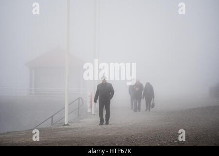 Aberystwyth, Pays de Galles, Royaume-Uni. 14Th Mar, 2017. Météo France : Les gens qui marchent le long de la promenade est obscurci par le brouillard dans la station balnéaire d'Aberystwyth, sur la côte ouest du pays de galles comme un épais manteau gris et froid de la brume de mer tourbillonnant en vient au large de la mer d'Irlande, cet après-midi. Crédit photo : Keith Morris/Alamy Live News Banque D'Images