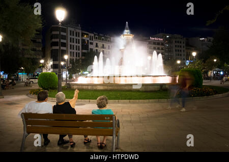 Trois personnes âgées s'asseoir sur un banc, dos à la caméra à la recherche à la fontaine illuminée sur la Plaza del Campilo un soir d'été à Grenade Espagne Banque D'Images