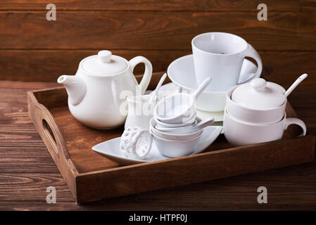 Ensemble de nouveaux plats blanc avec théière, tasses, assiettes et sur plateau en bois à une table en bois Banque D'Images