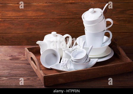 Ensemble de nouveaux plats blanc avec théière, tasses, assiettes et sur plateau en bois à une table en bois Banque D'Images