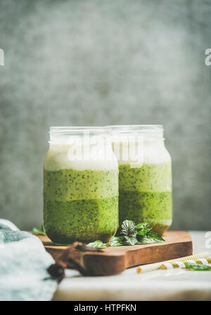 Ombre verte avec des smoothies en couches dans des bocaux en verre de menthe sur planche de bois, mur de béton gris, l'arrière-plan copie espace, selective focus. Manger végétalien, propre Banque D'Images