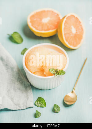 Sorbet pamplemousse rose à la menthe fraîche dans un bol blanc sur fond peint bleu, selective focus. Frais sain concept dessert d'été végétalien premières Banque D'Images