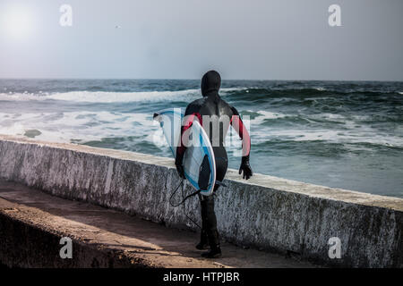 Les jeunes surfeurs musclés s'exécute dans l'eau de porter une combinaison isothermique en hiver. Cold wind surf. Splash vague sur l'arrière-plan. Il a combinaison imperméable Banque D'Images