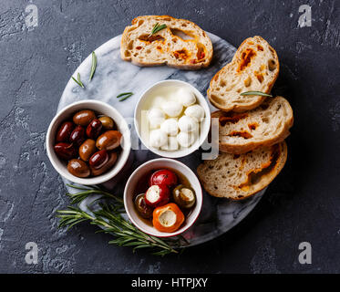 Les olives, les poivrons farcis, mini-mozzarella et tranches de pain ciabatta sur fond sombre Banque D'Images
