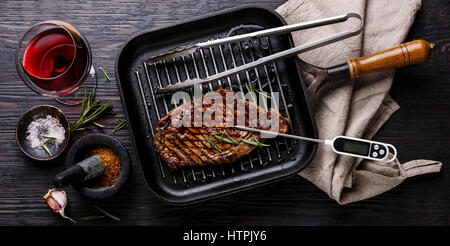 Faux filet entrecôte grillée sur pan et thermomètre à viande sur fond de bois brûlé noir Banque D'Images