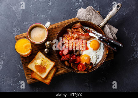 Le petit déjeuner anglais en plat de cuisson avec les œufs, saucisses, bacon, haricots, des toasts et du café à l'arrière-plan en pierre sombre Banque D'Images