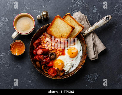 Le petit déjeuner anglais en plat de cuisson avec les œufs, saucisses, bacon, haricots, des toasts et du café à l'arrière-plan en pierre sombre Banque D'Images