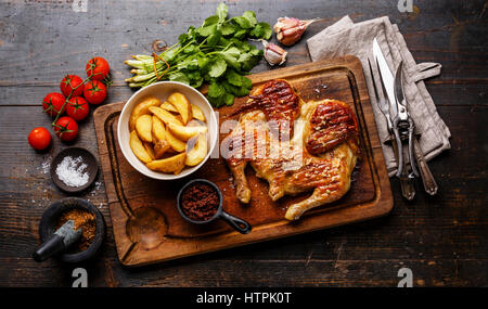 Poêlée de poulet grillé rôti Tabaka et les quartiers de pommes de terre sur une planche à découper sur fond de bois Banque D'Images