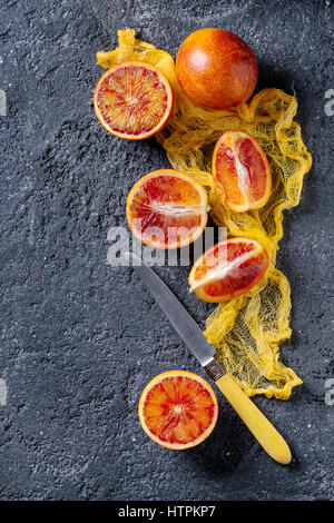 Tout en tranches et d'orange sanguine de Sicile juteuse à maturité des fruits avec le couteau et le textile jaune sur fond noir texture béton. Vue de dessus avec l'espace Banque D'Images