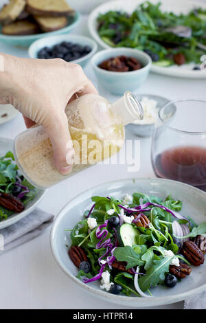 Verser la vinaigrette au feta grillée Sherry Noyer sur un pacanes épicées salade Feta servi avec du pain et du vin rouge. Photographié sur un bac blanc Banque D'Images