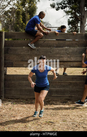 Woman running tout en aidant les hommes à monter formateur un mur en bois au cours de parcours Banque D'Images