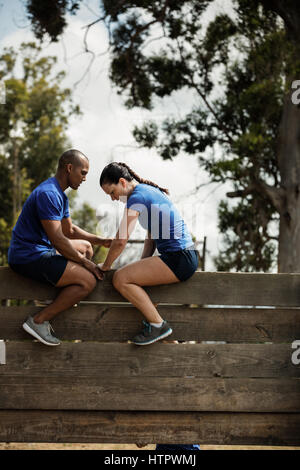 Male trainer assisting woman d'escalader un mur en bois au cours de parcours Banque D'Images