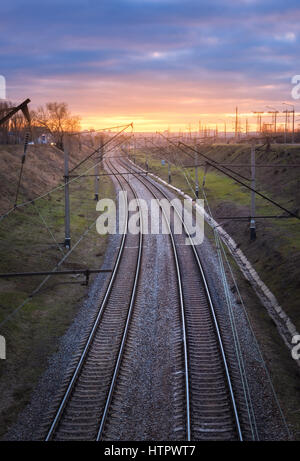 Belle vue depuis le pont sur le chemin de fer au coucher du soleil. Paysage industriel colorés avec gare, ciel nuageux bleu et jaune du soleil. Rai Banque D'Images