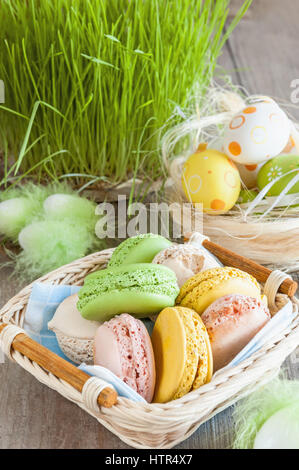 Macarons meringues multicolores dans un panier en osier d'œufs de Pâques sur un fond d'herbe pour Pâques Banque D'Images