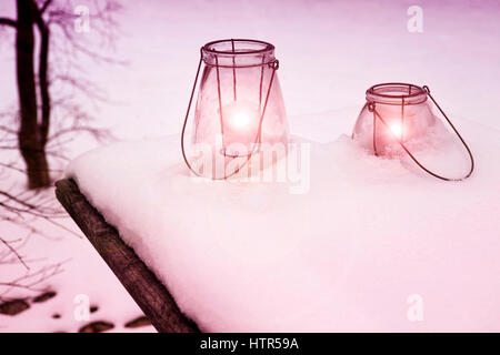 Deux de verre avec des bougies allumées dans la neige Banque D'Images