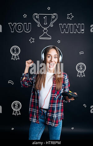 Ma victoire. Contenu joyeux young woman smiling et gagner un tour dans les jeux vidéos tout en jouant les jeux vidéos Banque D'Images