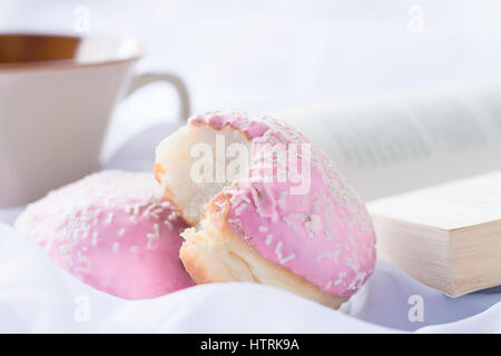 Deux beignes glacés rose avec sprinkles, tasse à café et d'adresses, sur un fond soyeux blanc Banque D'Images