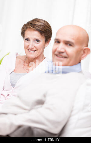 Happy middle-aged couple relaxing at home sur un canapé tournant de sourire à l'appareil photo avec l'accent de la jolie femme Banque D'Images