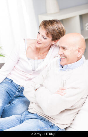 Happy casual couple relaxing regarder la télévision ensemble sur un canapé à la maison en souriant avec plaisir dans une vue de côté Banque D'Images