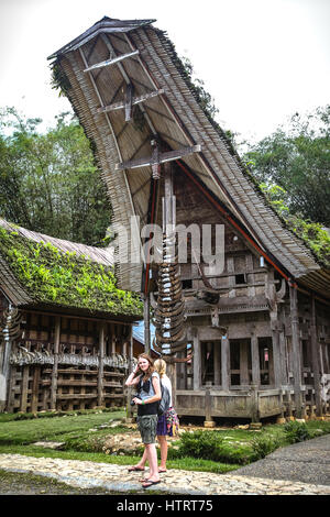 Touristes se tenant en face du bâtiment traditionnel Tongkonan à Kete Kesu, Nord de la Toraja, Sud Sulawesi, Indonésie. Banque D'Images