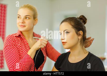 Ce maître du maquillage à l'aérographe d'une jeune fille dans un salon de beauté. Blonde and brunette femmes. Banque D'Images