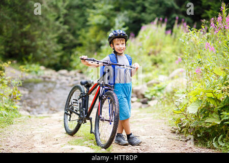 Petit garçon souriant casque de vélo de montagne avec commandes sur le sentier Banque D'Images