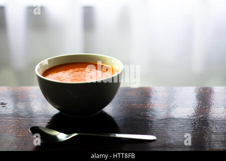 Photo d'une mugir de soupe de tomate avec une cuillère sur le côté assis sur une planche en bois Banque D'Images