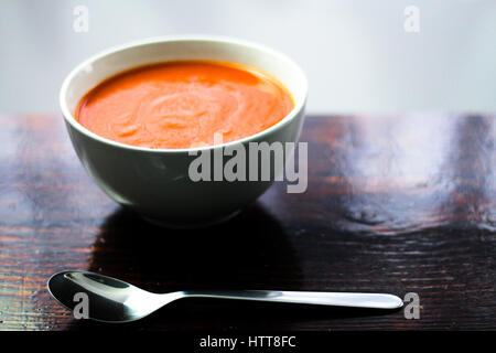 Photo d'une mugir de soupe de tomate avec une cuillère sur le côté assis sur une planche en bois Banque D'Images