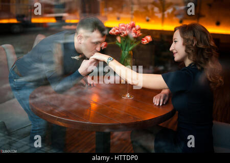 Bisous jeune homme femme par la main et lui fait la proposition de mariage. Voir à travers le verre. Ils sont assis à table à côté de verres de vin et l'esprit Banque D'Images