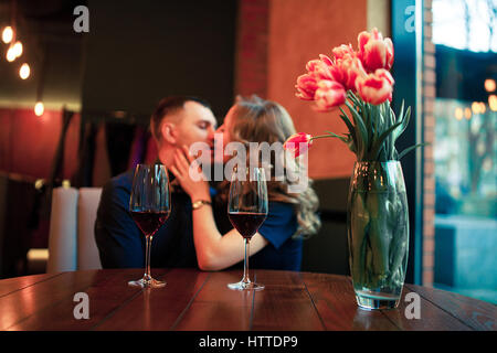 Jeune homme faite par femme proposition de mariage et ils s'embrassent. Ils sont assis à table à côté de verres de vin et vase avec fleurs. Banque D'Images