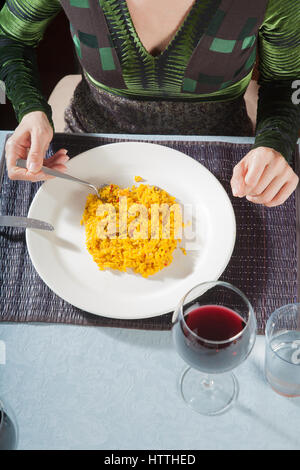 Vue aérienne de femme avec robe vert manger la paella, plat de riz typique espagnol, avec la fourchette dans un plat blanc au tableau de restaurant Banque D'Images