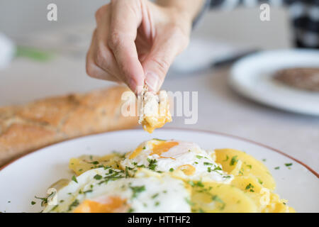 Femme part avec morceau de pain frit trempant dans de l'œuf œuf d'une cuisine typiquement espagnole, avec des tranches de pommes de terre sautées, et le persil haché Banque D'Images