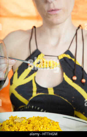 Femme avec robe jaune et marron avec fourche montrant la paella, plat de riz typique espagnol Banque D'Images