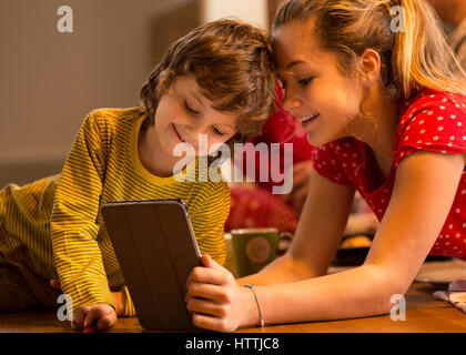 Frère et soeur de regarder quelque chose sur une tablette numérique ensemble. Ils sont couchés sur le plancher à la maison. Banque D'Images