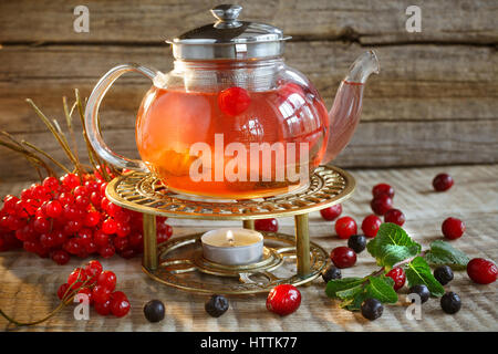 Tisane dans un pot de thé en verre. Plateau avec guelder rose, framboise. Banque D'Images