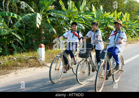 BEN TRE, VIET NAM- MAR 24 : groupe de trois élèves asiatiques non identifiés circuler à bicyclette sur les routes de campagne, d'aller à l'école, le garçon en uniforme avec l'amitié Banque D'Images