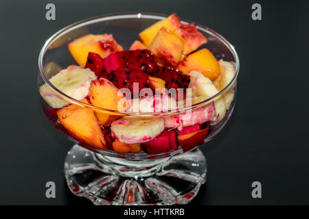 Salade de fruits sur fond sombre, pêches, bananes, fruit du dragon Banque D'Images