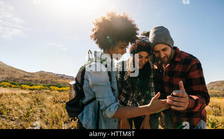 Trois jeunes randonneurs regardant des images sur téléphone mobile. Les jeunes de la randonnée dans la campagne. Banque D'Images