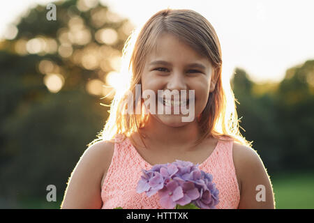 Portrait of a cute little girl smiling debout à l'extérieur dans un jardin tenant un bouquet de fleurs sauvages violet dans ses mains Banque D'Images